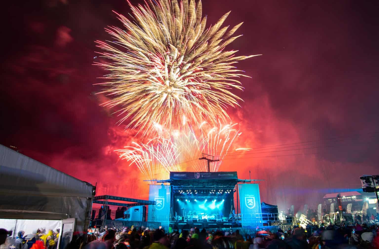 Colorful fireworks explode over a concert stage with a crowd below.