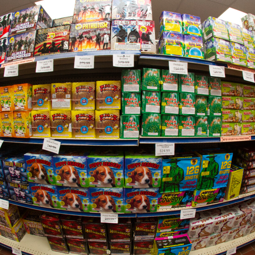 A shelf stocked with various colorful fireworks packaging and prices displayed.